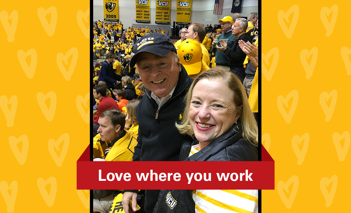 Tom and Kathleen Burke at a VCU basketball game with a red banner and white text that reads “Love where you work”