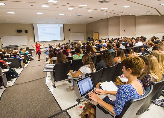 Lecture hall full of students, teacher presenting at the front of the hall