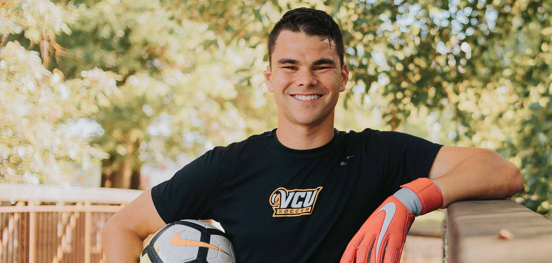 Mario wearing a VCU Soccer T-shirt and goalkeepr gloves. Holding a soccer ball at his side.