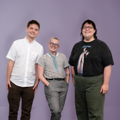 Three people standing against a purple wall