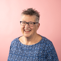 A woman wearing  a blue blouse against a pink-ish background